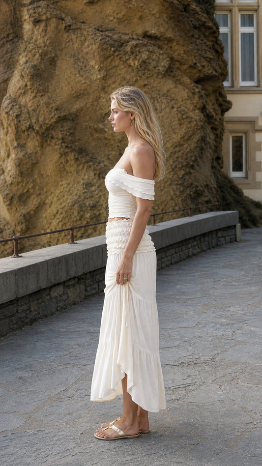 Side profile view of woman in ivory two-piece set standing near stone wall