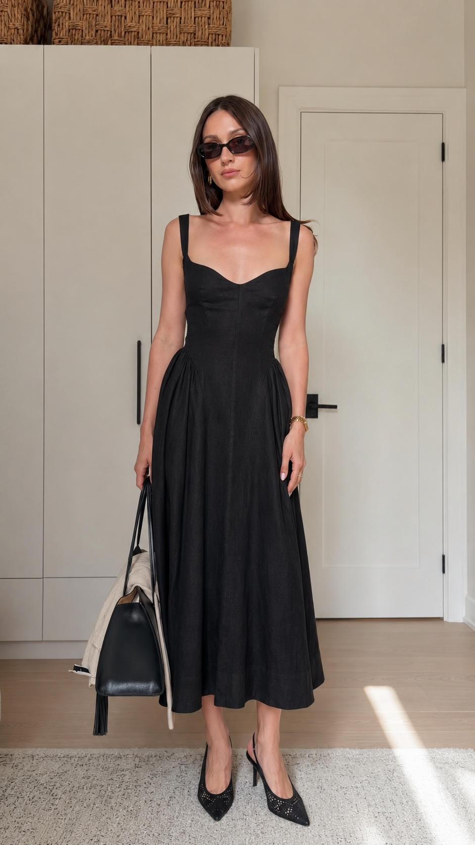 Model wearing a black sleeveless sweetheart neck midi dress styled with pointed heels